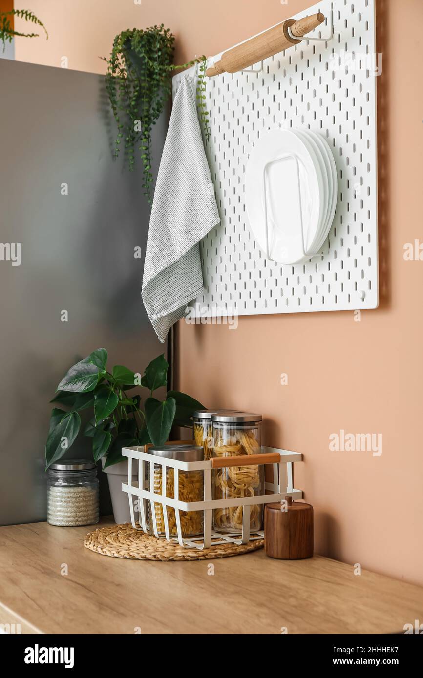 Jars on wooden counter and pegboard with kitchen utensils on color wall