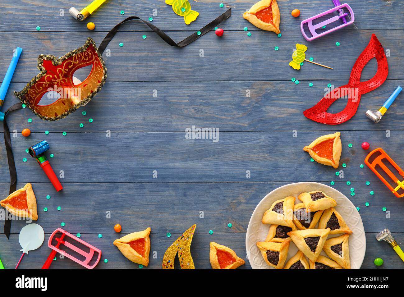 Frame made of party decor and Hamantaschen cookies with rattles for Purim holiday on color wooden background Stock Photo