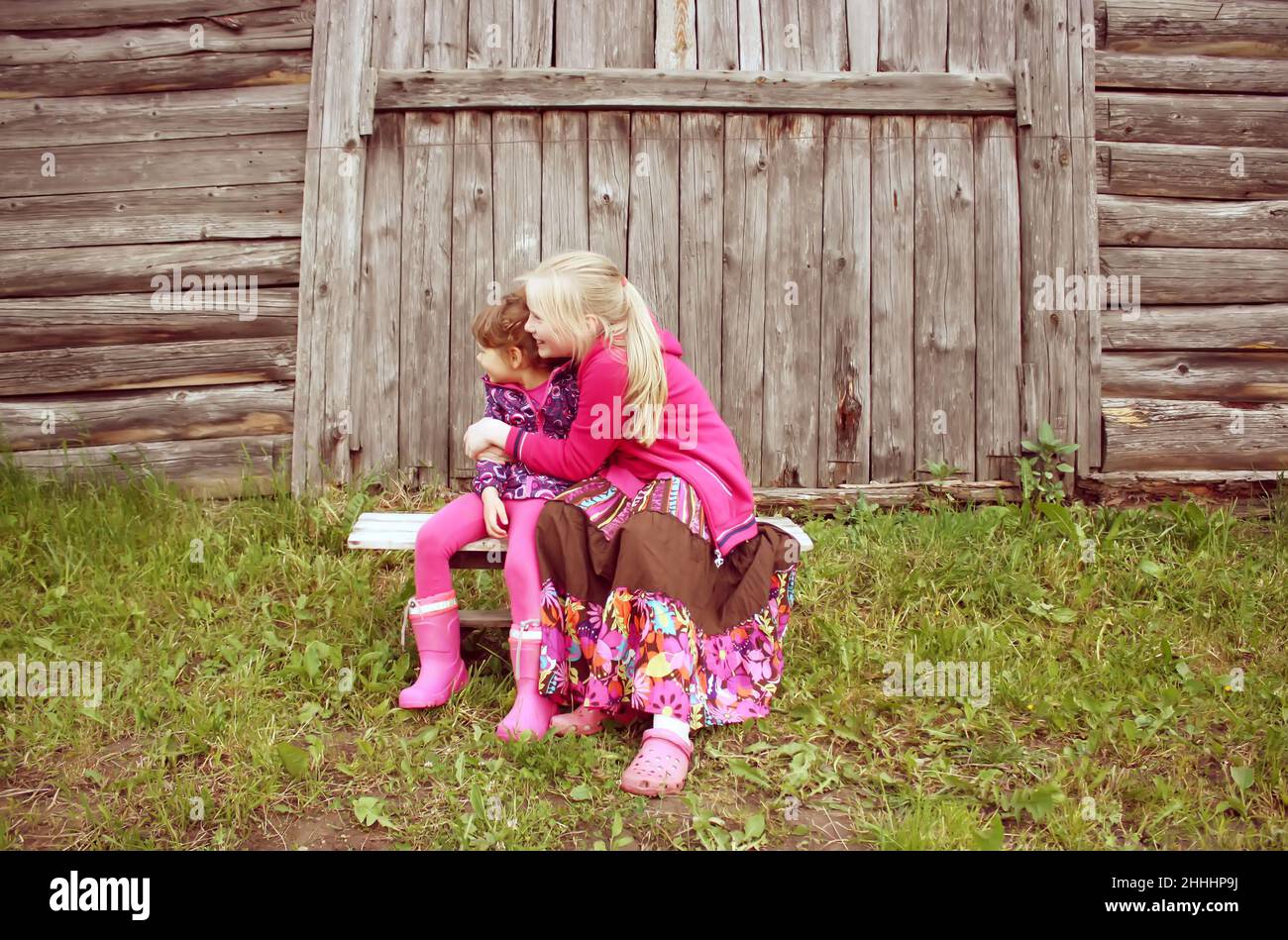 Two adorable girls sitting on the wooden bench on old wooden wall ...
