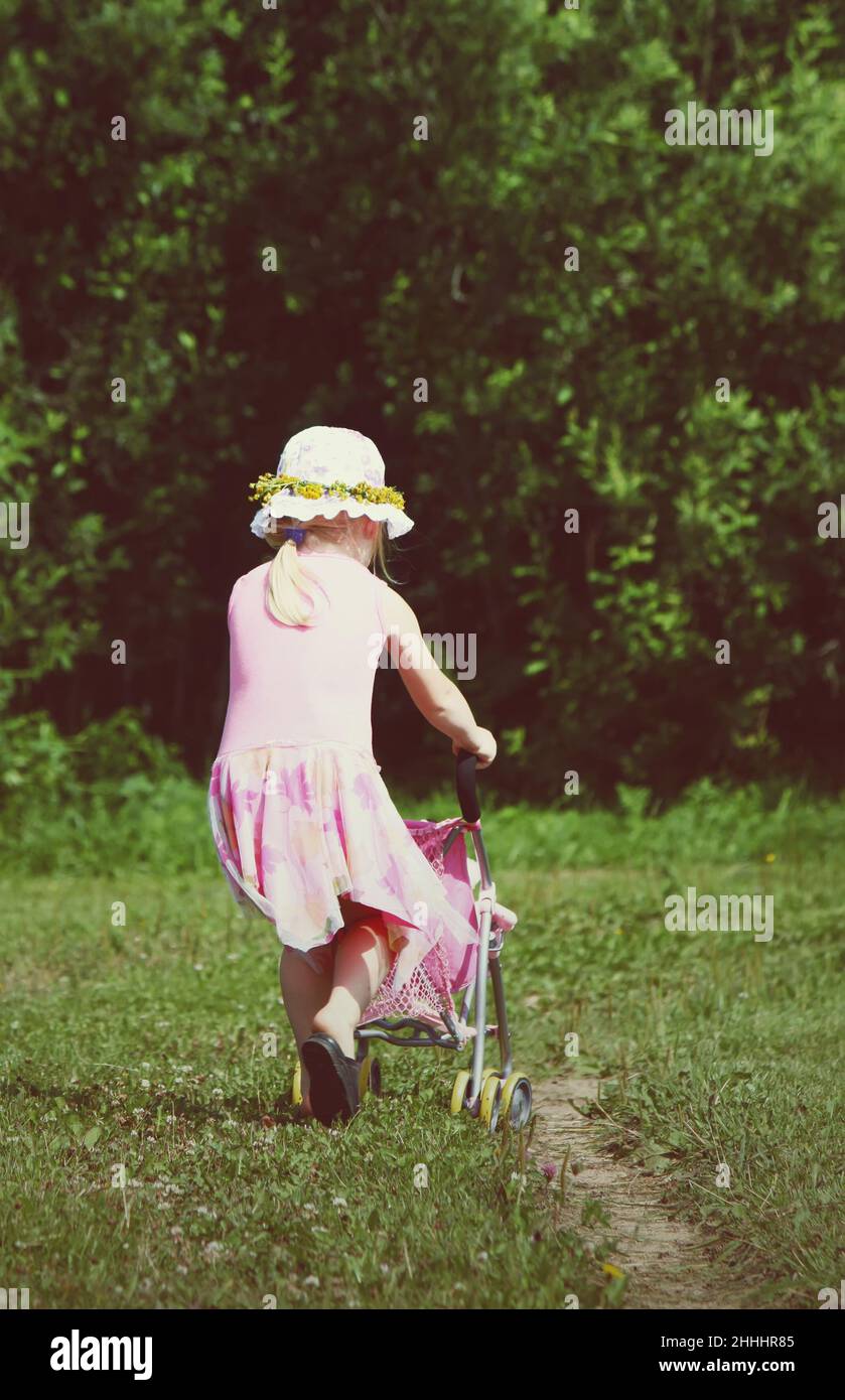 Cute little girl playing with her baby carriage outdoors. Stock Photo
