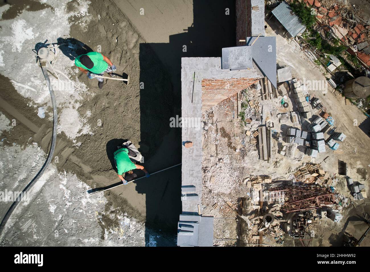 Two men builders screeding floor at construction site. Top view of male worker standing near concrete screed mixer machine and holding shovel while colleague using leveling surface with straight edge. Stock Photo