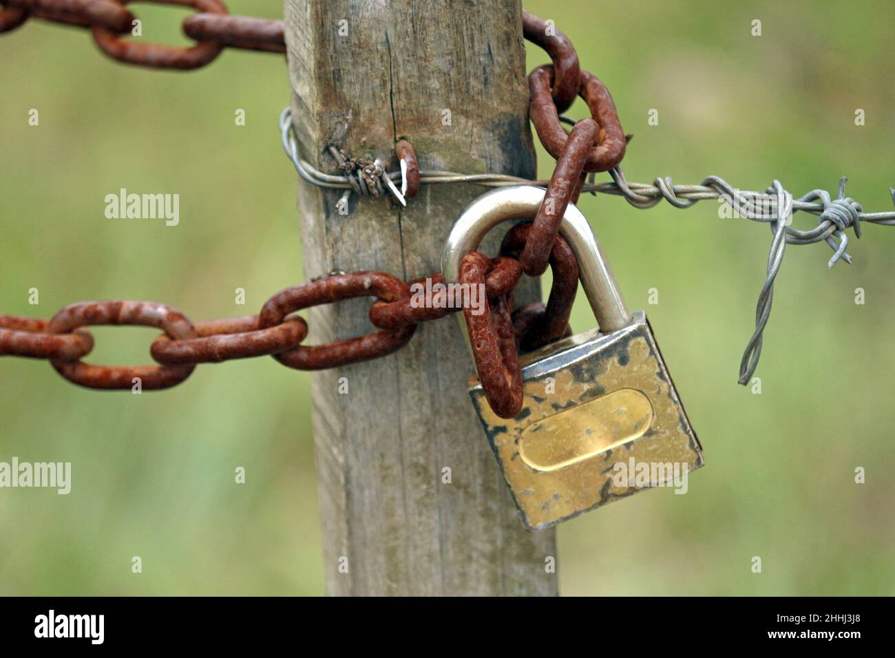 A small wooden pole suspended by barbed wire, a rusty chain and a small padlock. In the simple life of the countryside there are no walls. Stock Photo