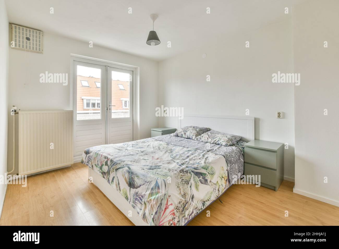 Interior of a light bedroom with white double bed ,grey cupboards and a