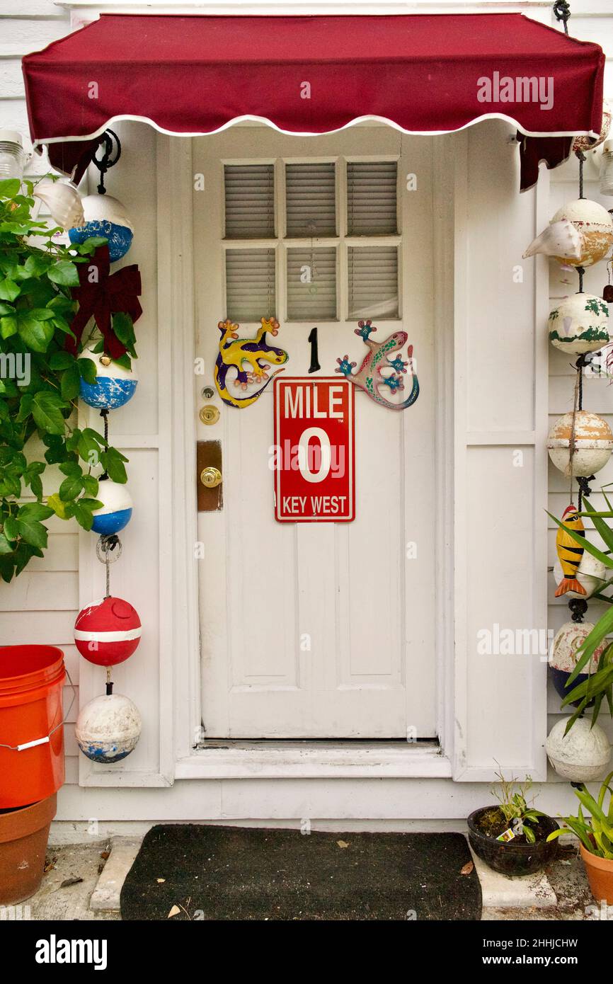 Front door with Mile Marker “0” and decorative geckos in Key West, Florida, FL, USA.  Hanging fishing buoys and a red awning surround the door.  Tropi Stock Photo