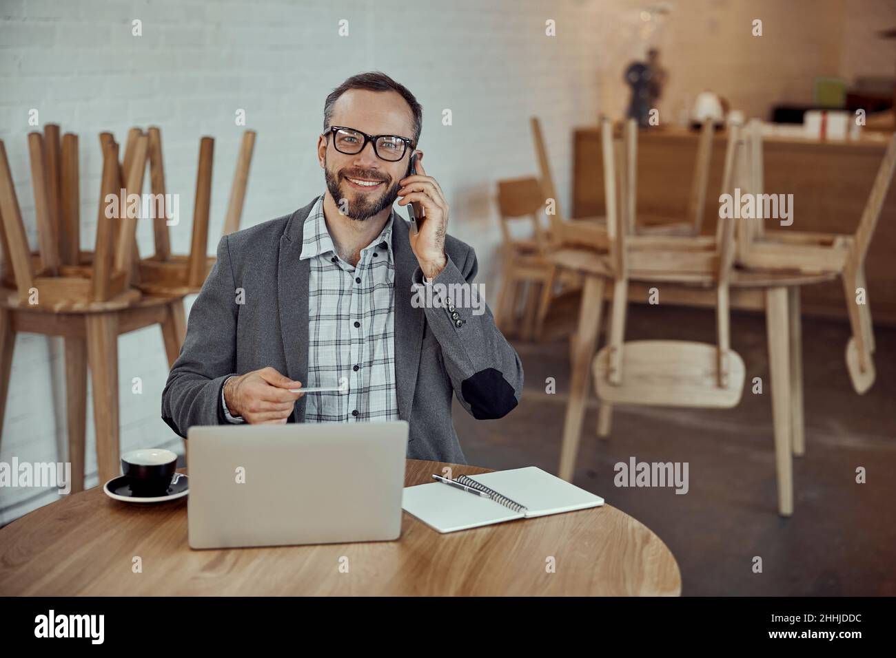 Joyful man using notebook and talking on cellphone in cafe Stock Photo