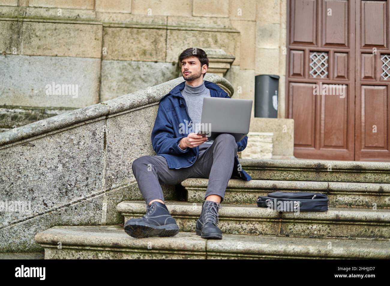 Male student sitting on stone staircase and browsing netbook while preparing for university task Stock Photo