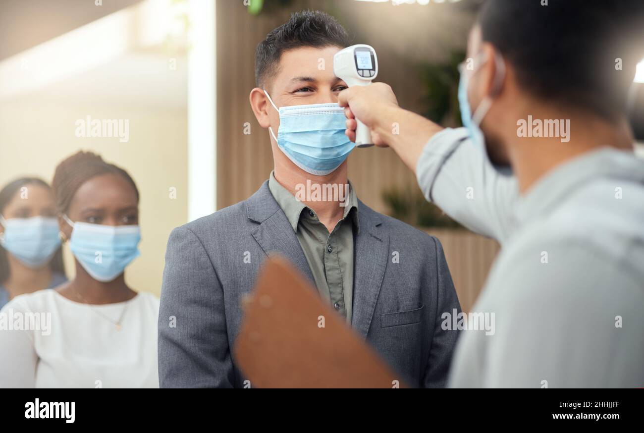 Lined up to be screened. Cropped shot of a handsome mature businessman wearing a mask and having his temperature taken while standing at the head of a Stock Photo
