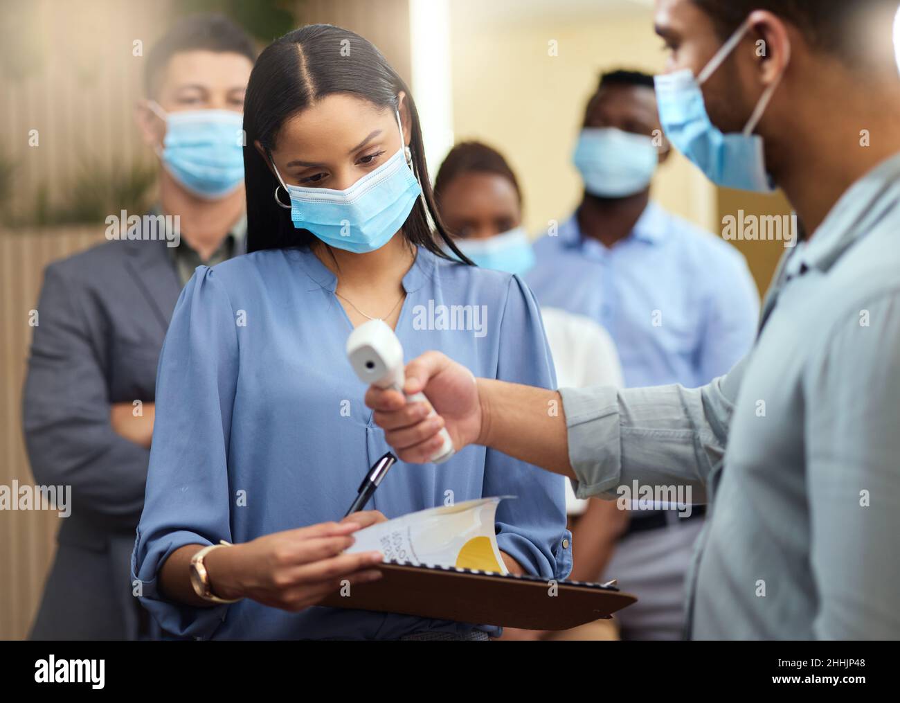 Your temperature looks good. Cropped shot of an attractive young businesswoman wearing a mask and going through covid screen while standing at the Stock Photo