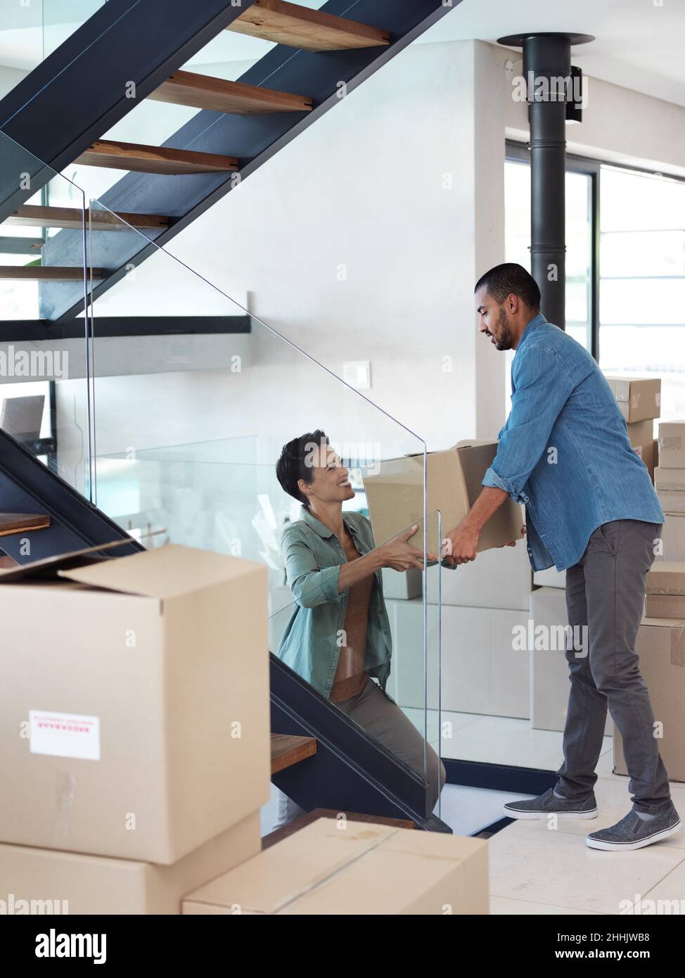 Is this the last of them. Shot of a happy young couple passing boxes to each other while moving into their new home. Stock Photo