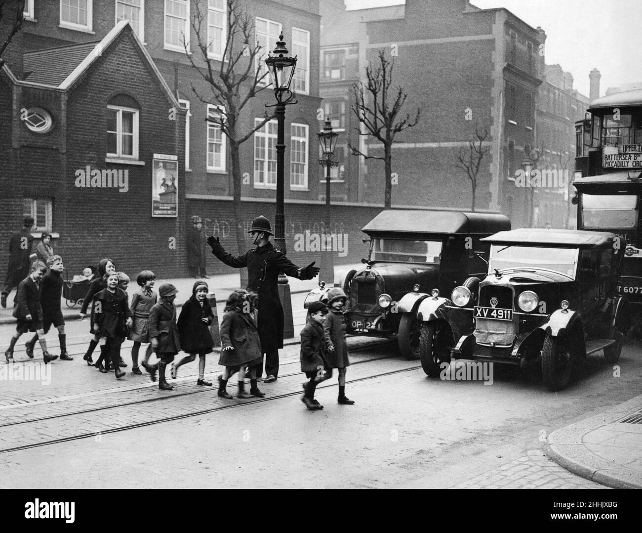 A policeman helping children to cross the road. London, February 1934. Stock Photo