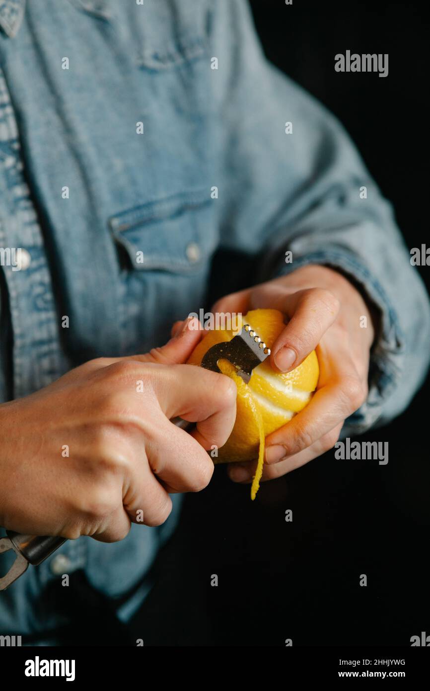 Cropped unrecognizable female bartender taking off lemon zest while preparing for making cocktail in bar during work Stock Photo