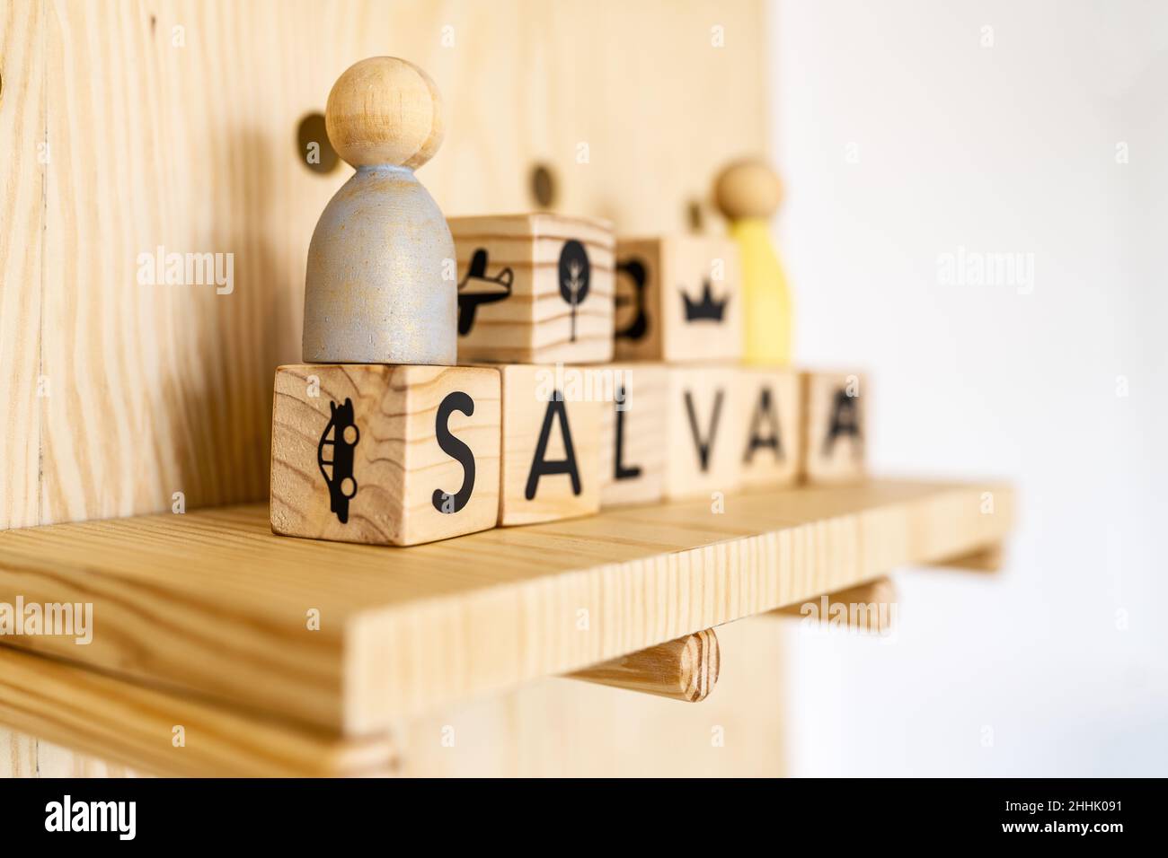 Baby name on toy wooden cubes placed on shelf with decorative elements at white wall in light playroom at home Stock Photo