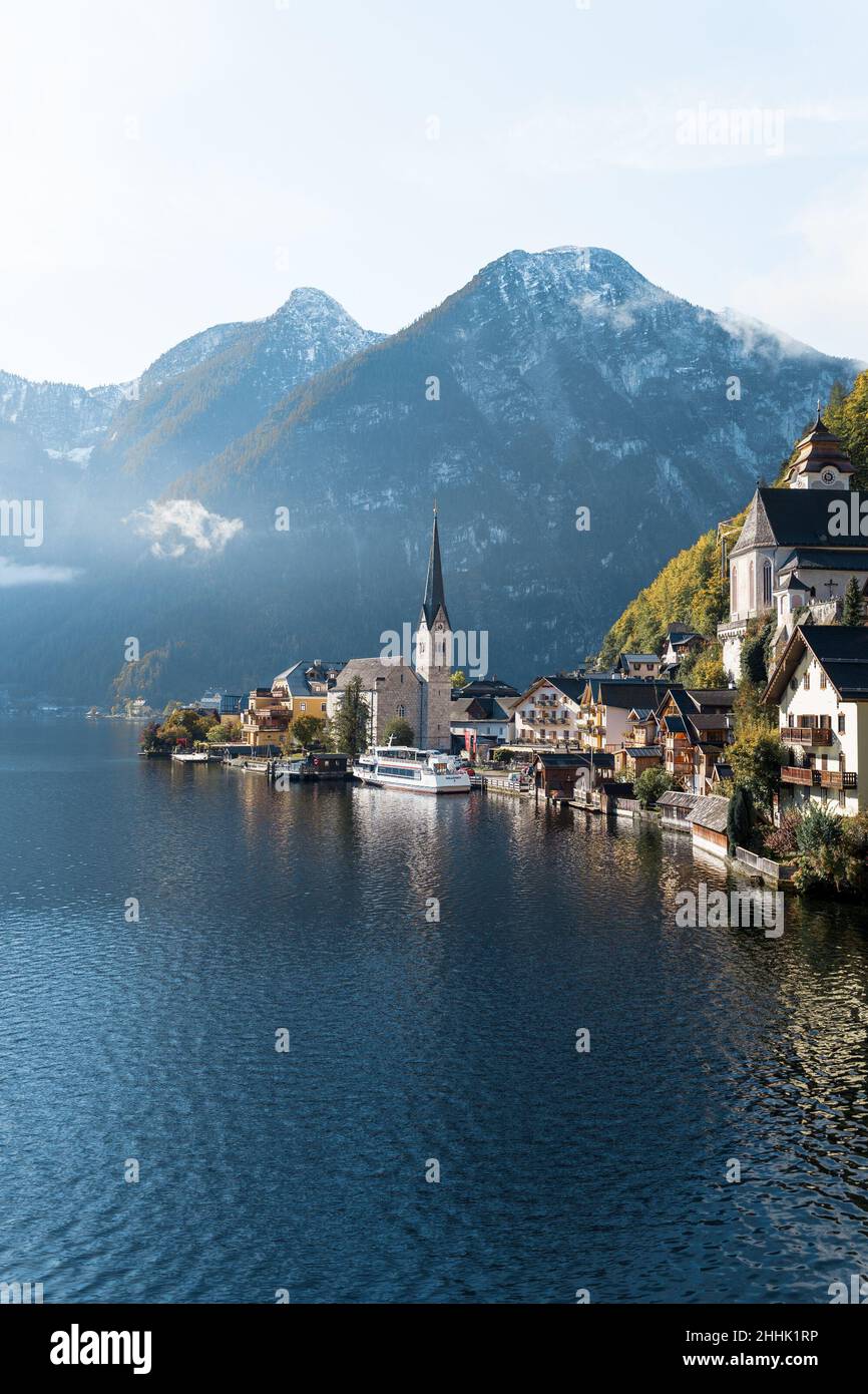 Picturesque view of small village located near calm lake surrounded by high mountains covered with coniferous forest in autumn sunny day in Austria ne Stock Photo