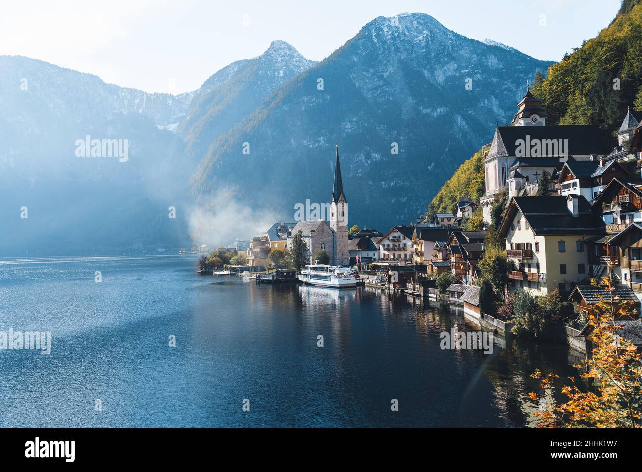 Picturesque view of small village located near calm lake surrounded by high mountains covered with coniferous forest in autumn sunny day in Austria ne Stock Photo