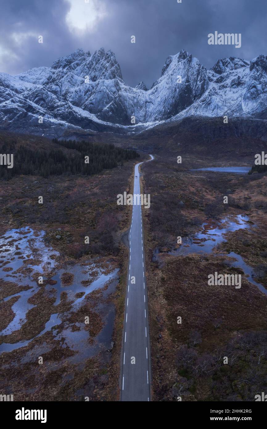 Aerial scenery of narrow asphalt road leading to snowy mountains in countryside under cloudy sky in Norway Stock Photo