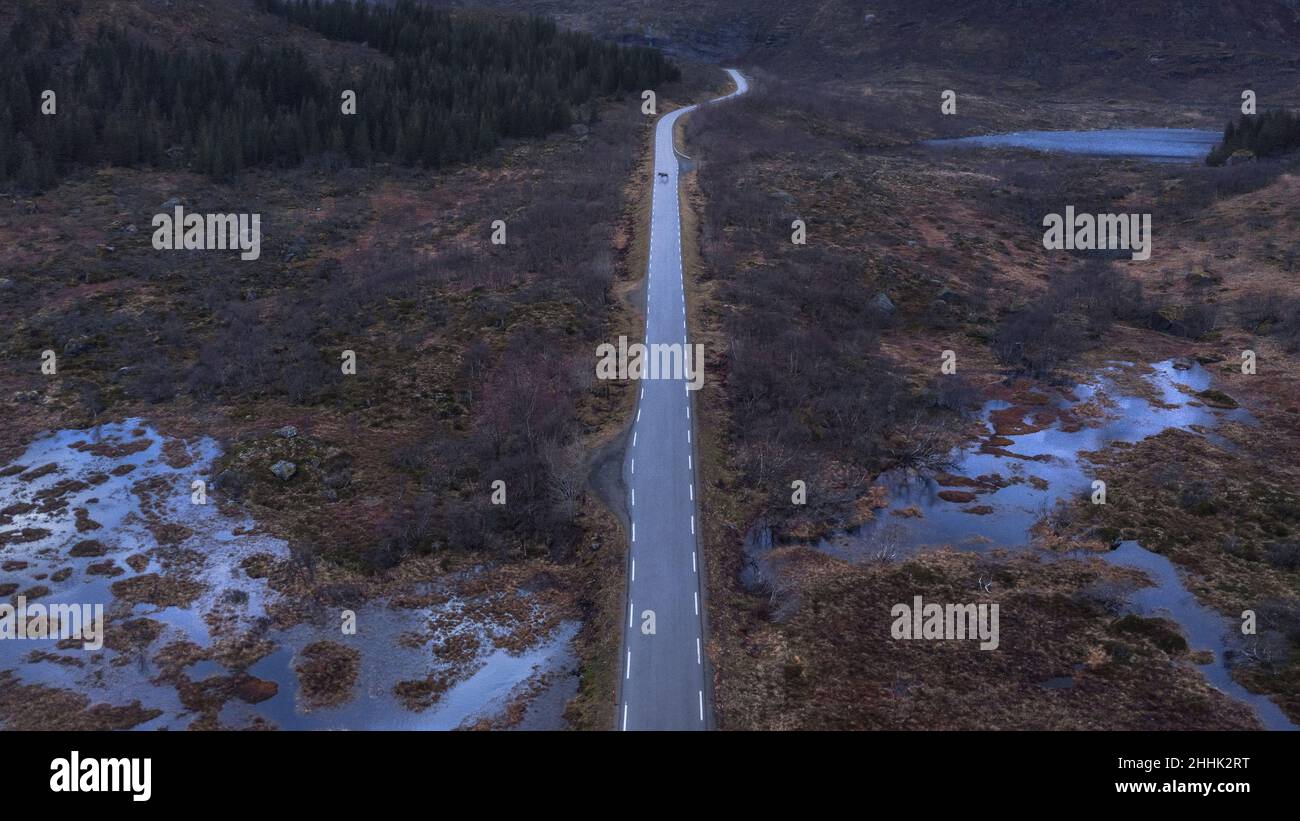 Aerial scenery of narrow asphalt road leading to snowy mountains in countryside under cloudy sky in Norway Stock Photo