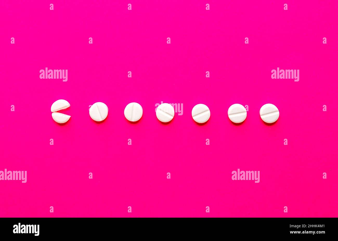 From above of broken and whole circle shaped pills placed in even line on vivid pink background in studio Stock Photo
