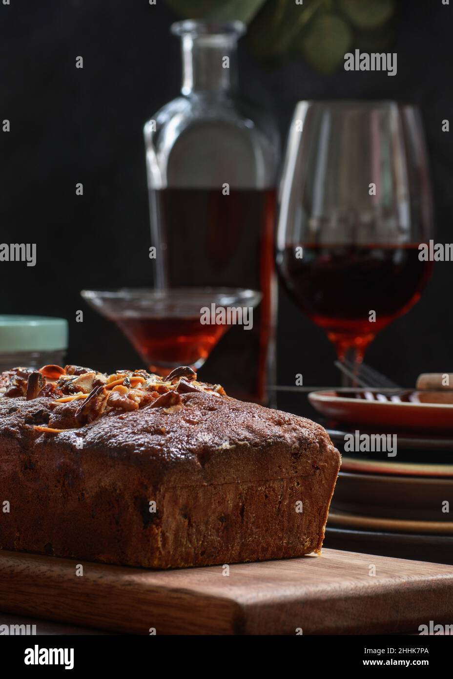 Tasty baked pound cake topped with almond flakes served on wooden cutting board on table with alcohol drink and berries Stock Photo
