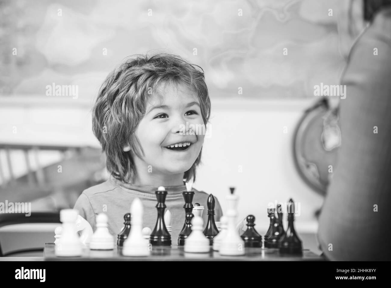 Young kid boy playing chess and having fun. Cheerful smiling little boy sitting at the table and evincing gladness while playing chess. Stock Photo