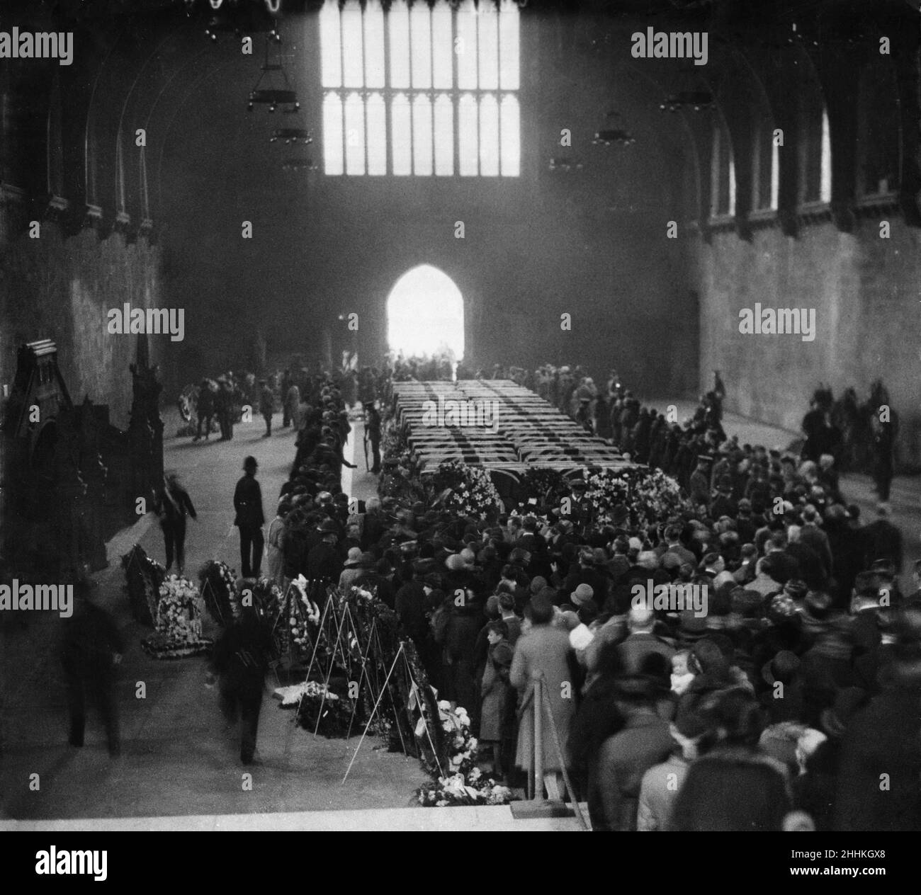 A Daily Mirror picture of the sad and impressive scene in historic Westminster Hall when the coffins of the forty-eight men killed in the R101 disaster lay in honoured state. An officer and men of the R.A.F., the latter with arms reversed, kept motionless guard beside the biers, around which were hundreds of beautiful wreaths, withthat sent by the King and Queen at the head. An endless stream of people, numbering many thousands, passed in silent homage through the dimly-lit hall and paused reverently around the coffins, each of which was covered with the Union Jack.  10th October 1930 Stock Photo