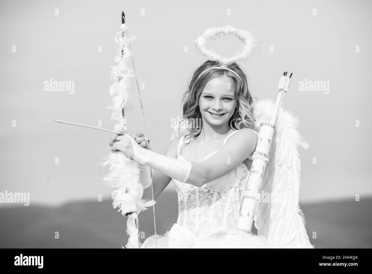 Innocent Girl With Angel Wings Standing With Bow And Arrow Against Blue Sky And White Clouds St