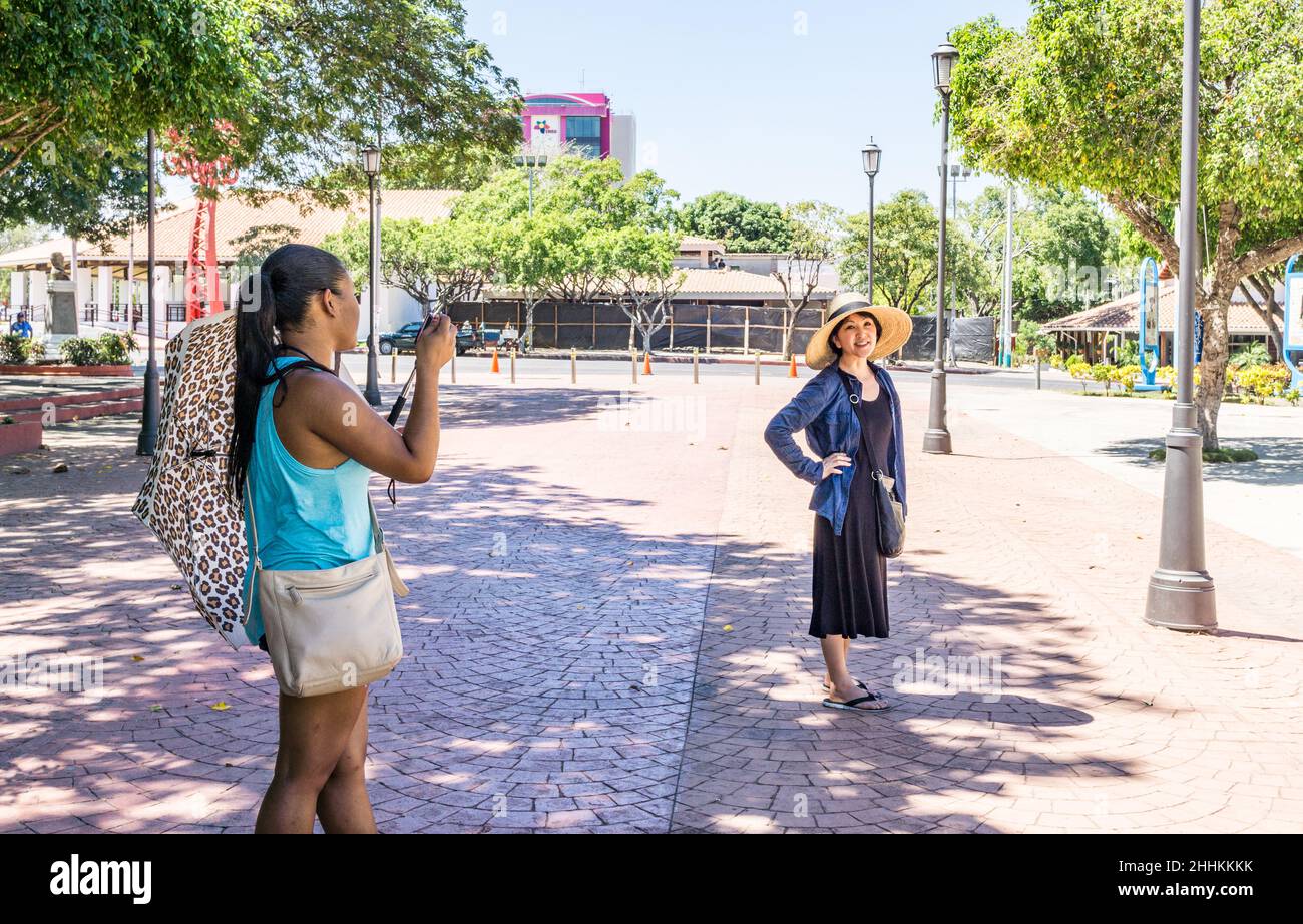 A Chinese woman posed for a Nicaraguan woman with cell phone camera in the Plaza de la Revolution, Managua, Nicaragua. Stock Photo