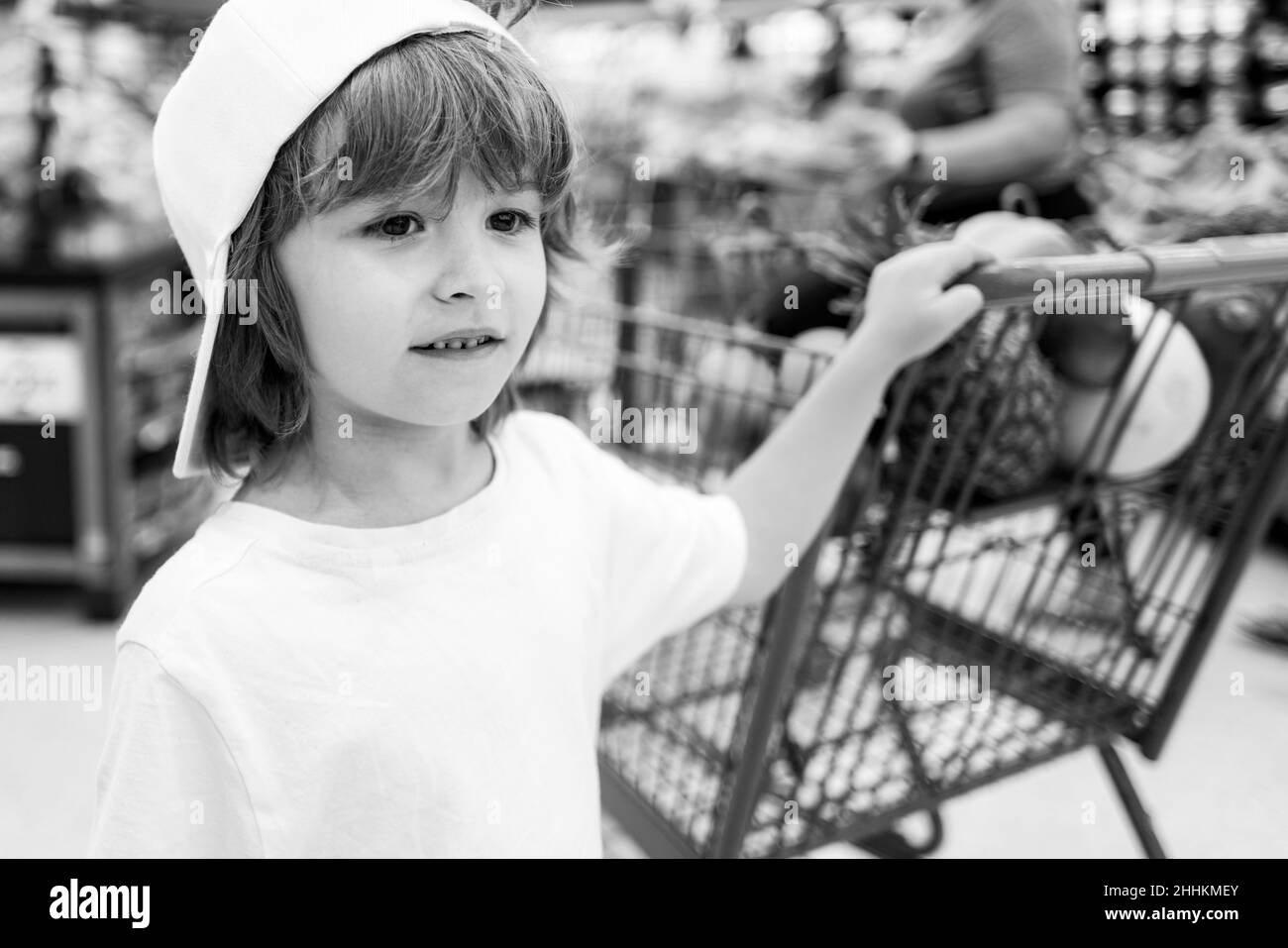 Sale, consumerism and people concept - happy little child with food in shopping cart at grocery store. Stock Photo