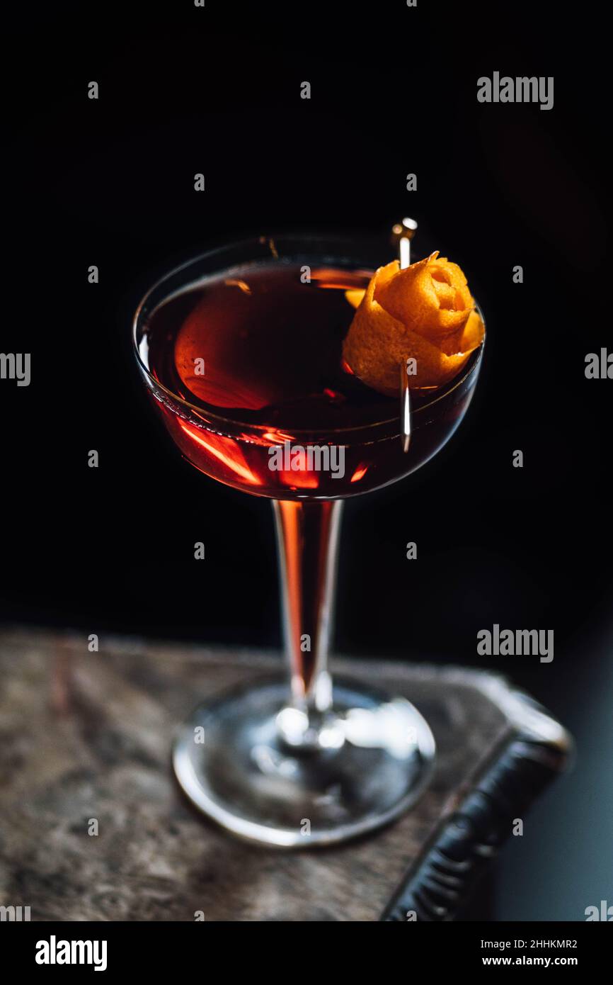 boulevardier cocktail in hollow stem glass with orange peel rose garnish against black Stock Photo