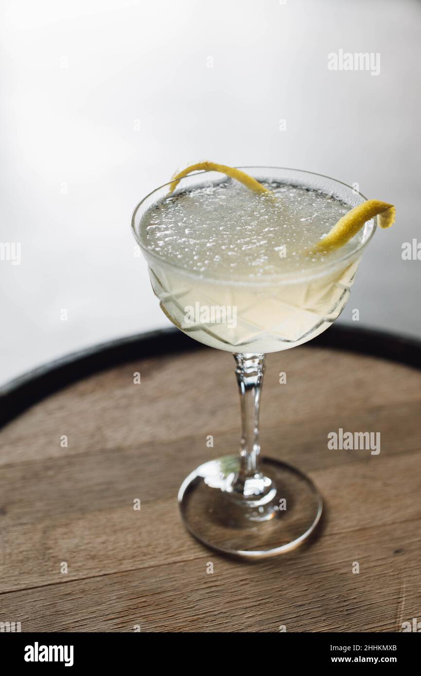 ice cold cocktail in champagne coupe glass stemware with lemon zest garnish on whiskey barrel Stock Photo
