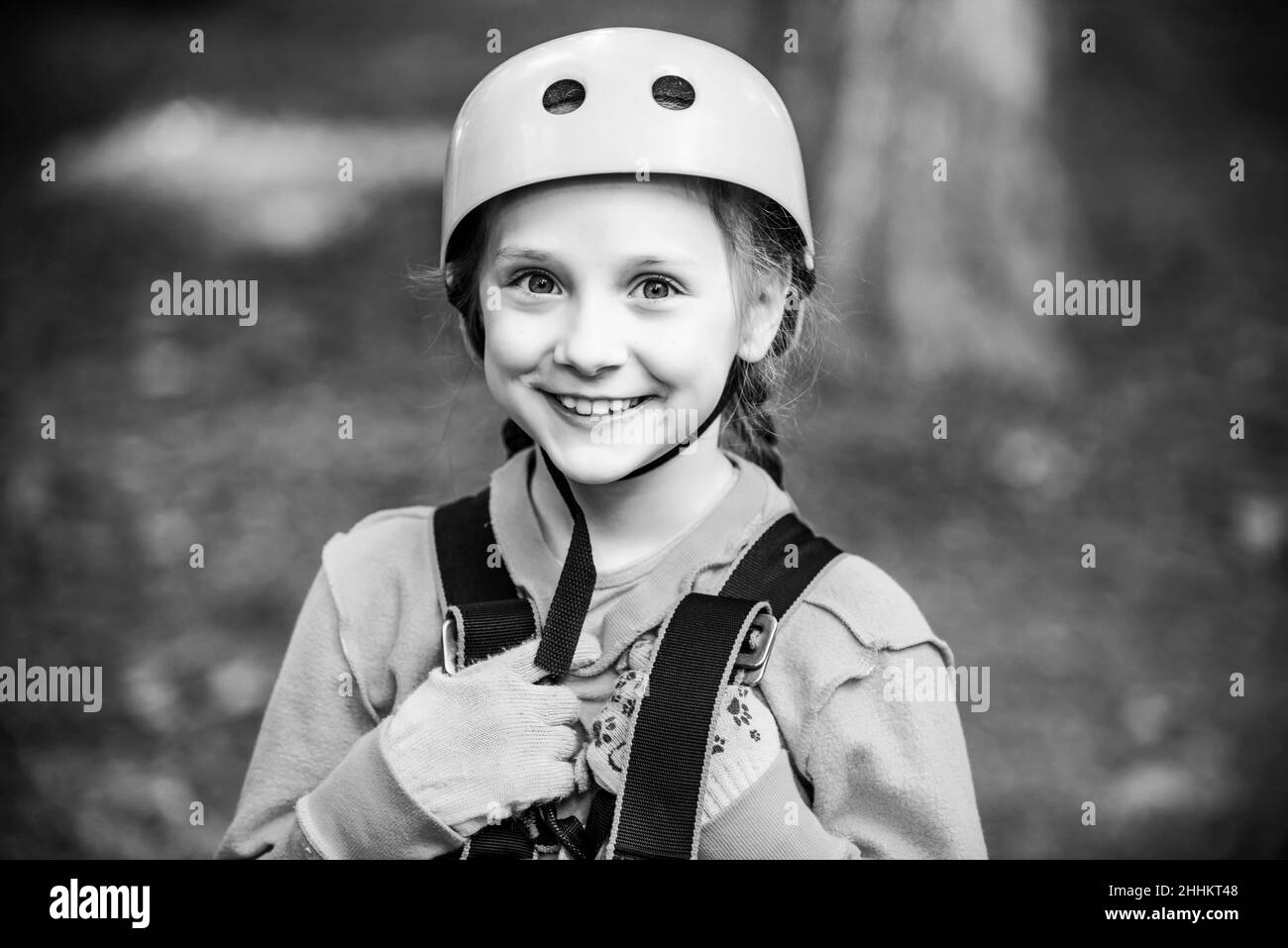 Cargo net climbing and hanging log. Cute child in climbing safety equipment in a tree house or in a rope park climbs the rope. Happy child in summer. Stock Photo