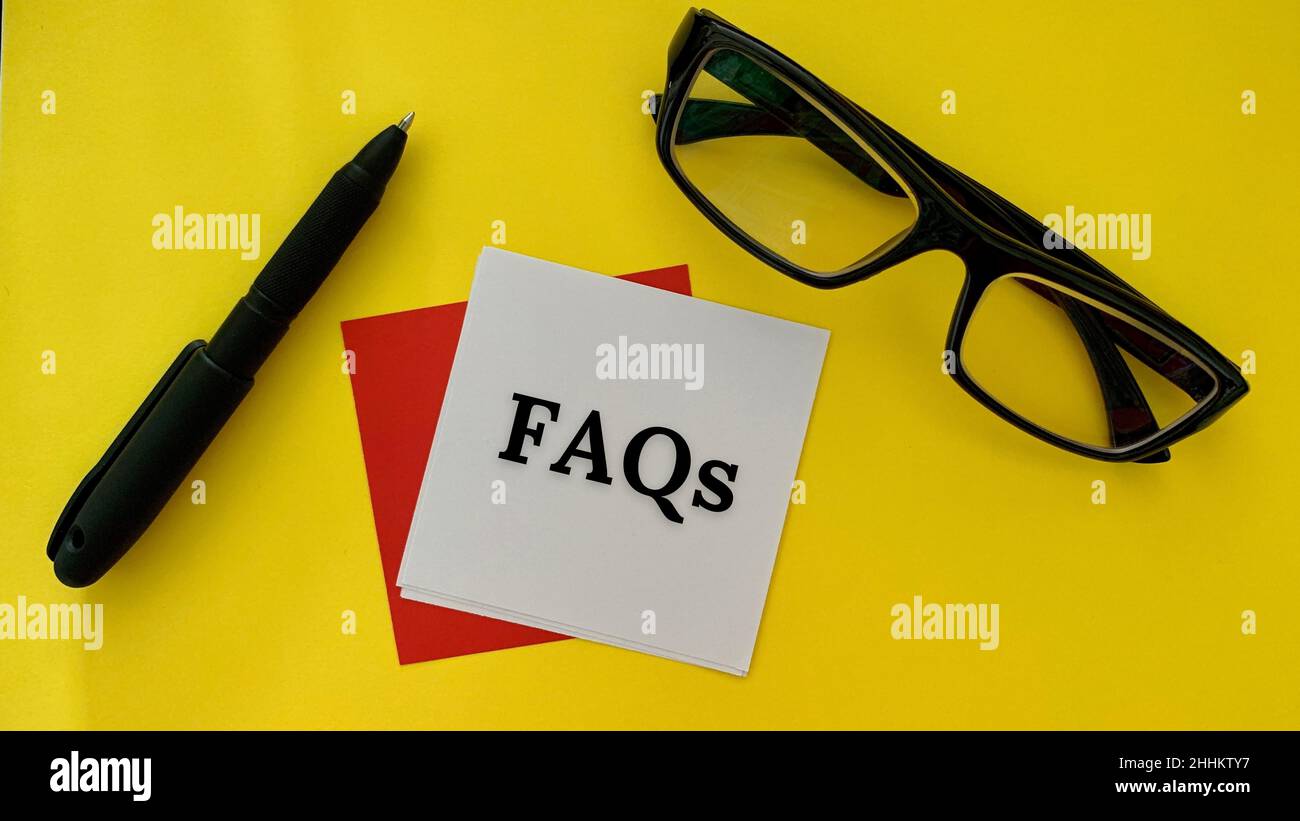 FAQs text on white post it note with pen, glasses and yellow background ...