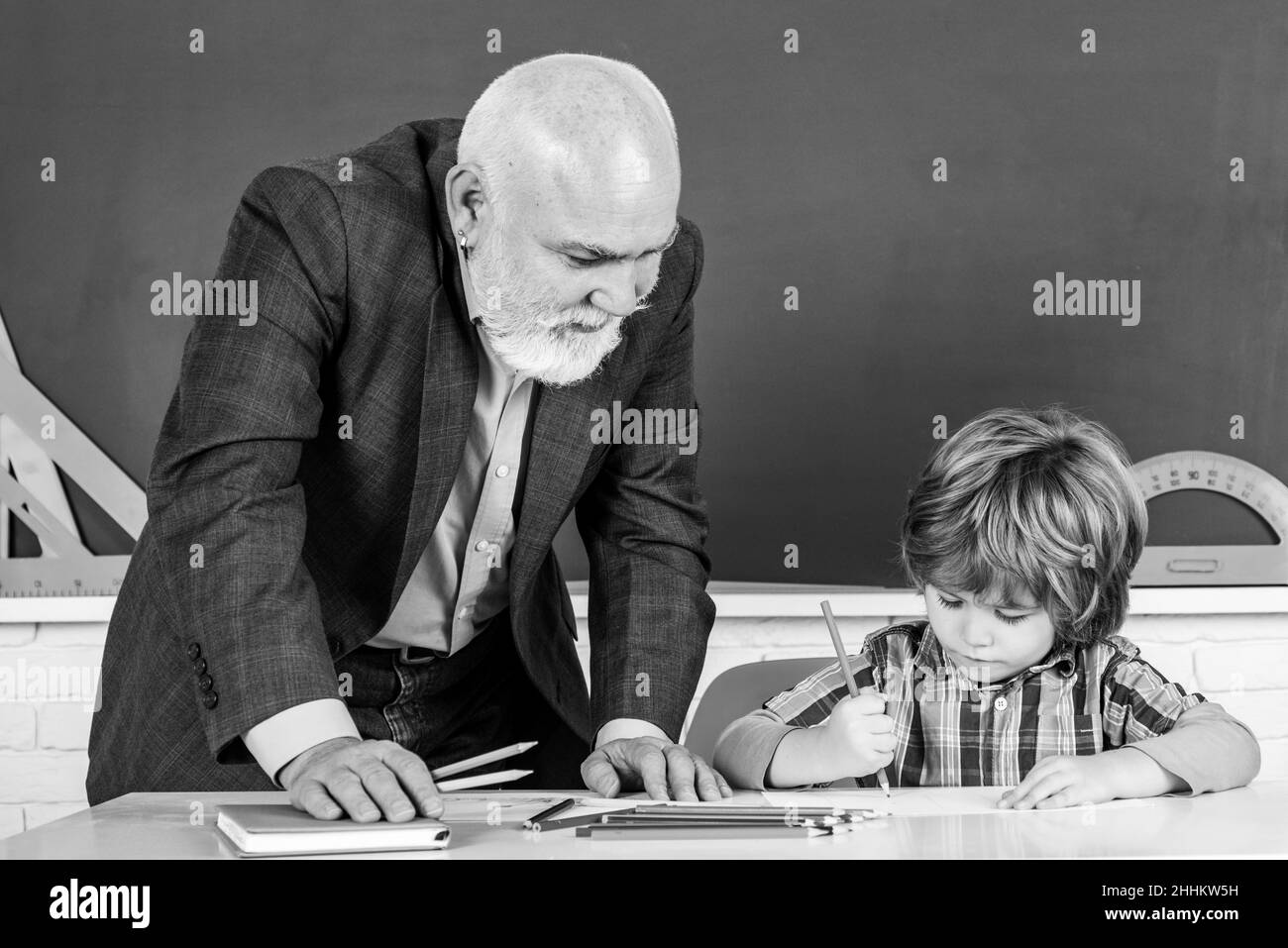 Senior teacher with pupil at back of classroom at the elementary school. Child at school lesson with senior teacher. Stock Photo