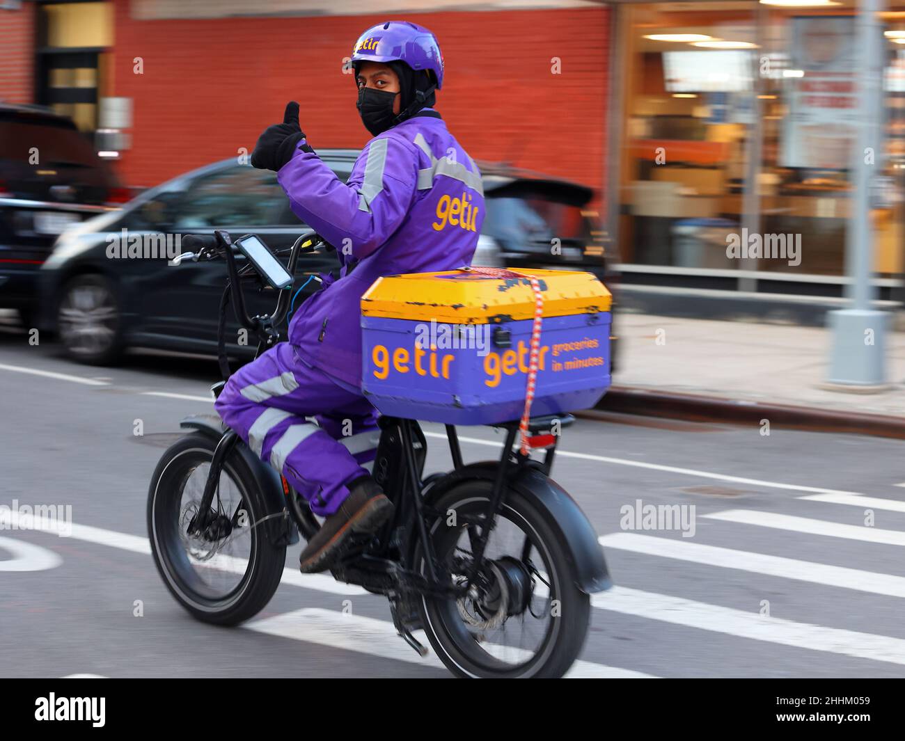 A Getir delivery person riding an e-bike gives a thumbs up as they drive past in New York City. motion blur. they are an instant needs quick commerce Stock Photo