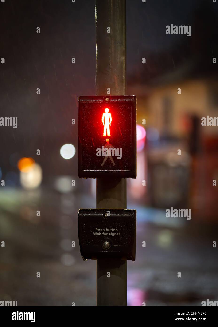 Red man stop sign illuminated at night on traffic light zebra crossing with road and streetlights out of focus behind. Pedestrians waiting for green Stock Photo