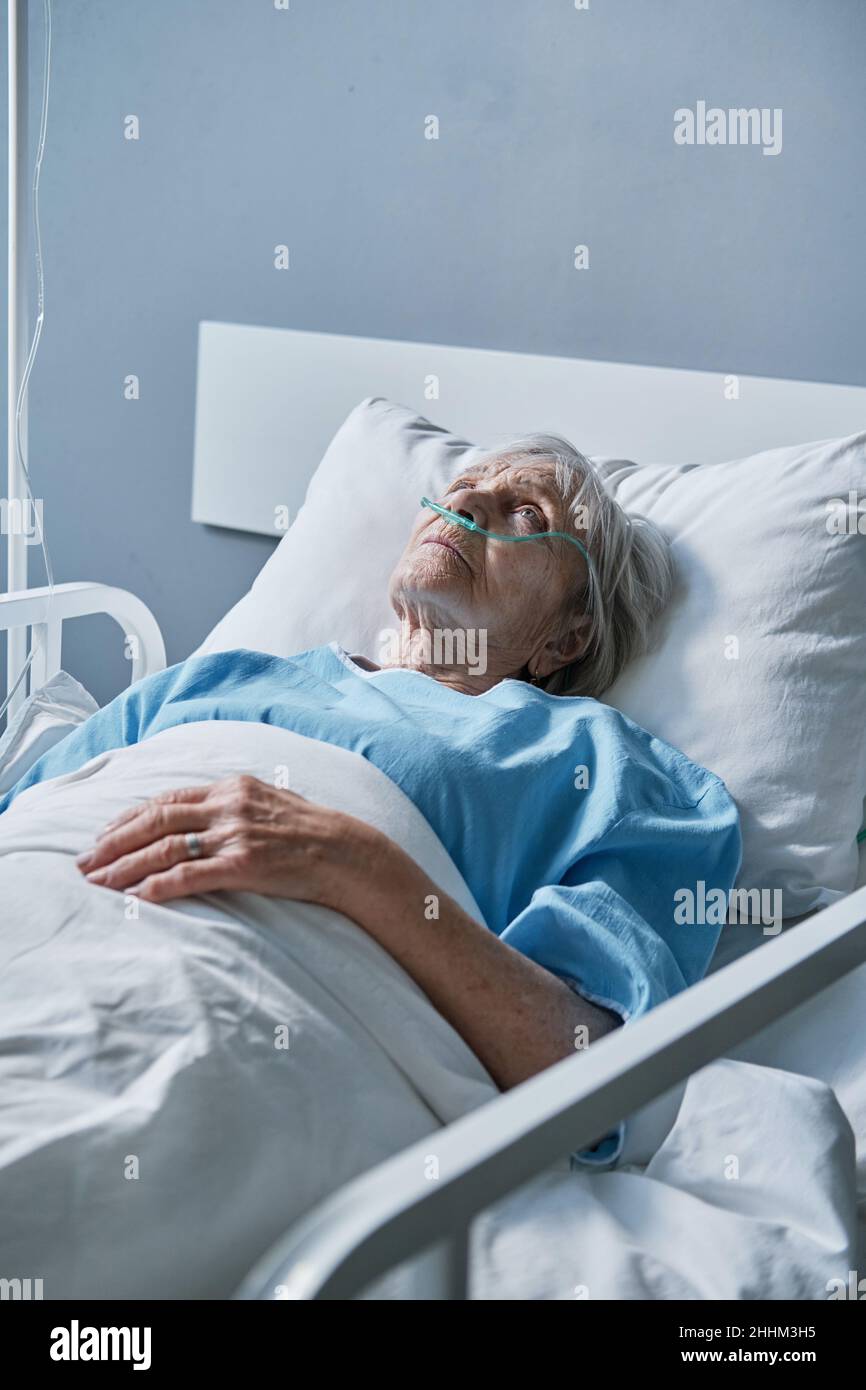 Senior woman with oxygen tube in her nose lying in bed at hospital ward