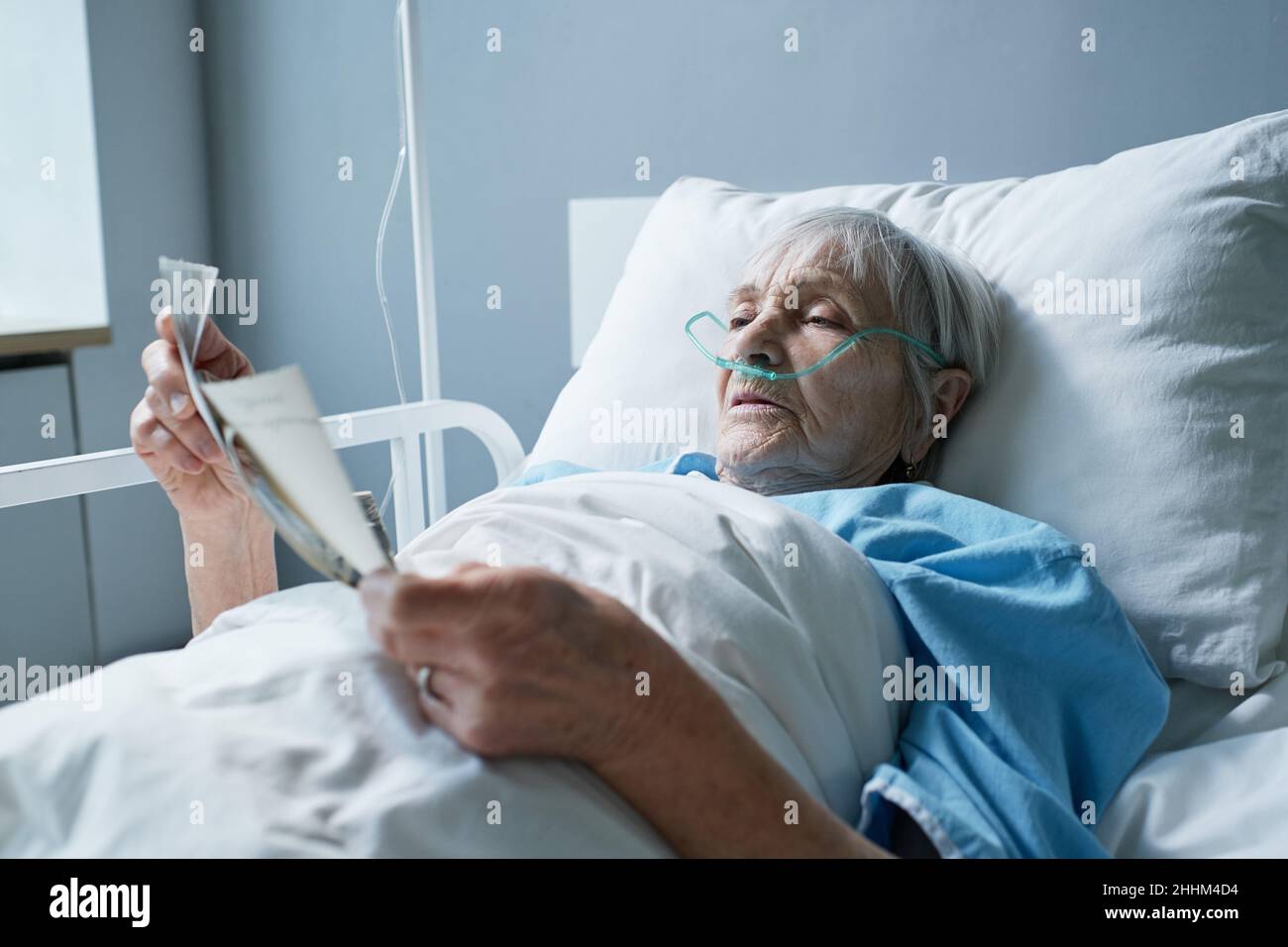 Sick senior woman lying on hospital bed with oxygen tube in her nose  remembering her past events by watching the old photos Stock Photo - Alamy