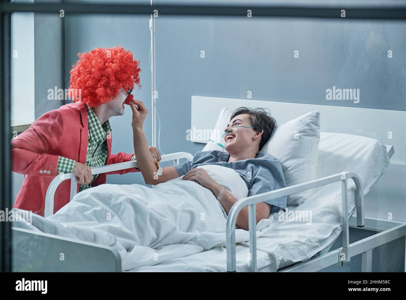 Young man dressing up in clown costume entertaining the sick woman at hospital ward Stock Photo