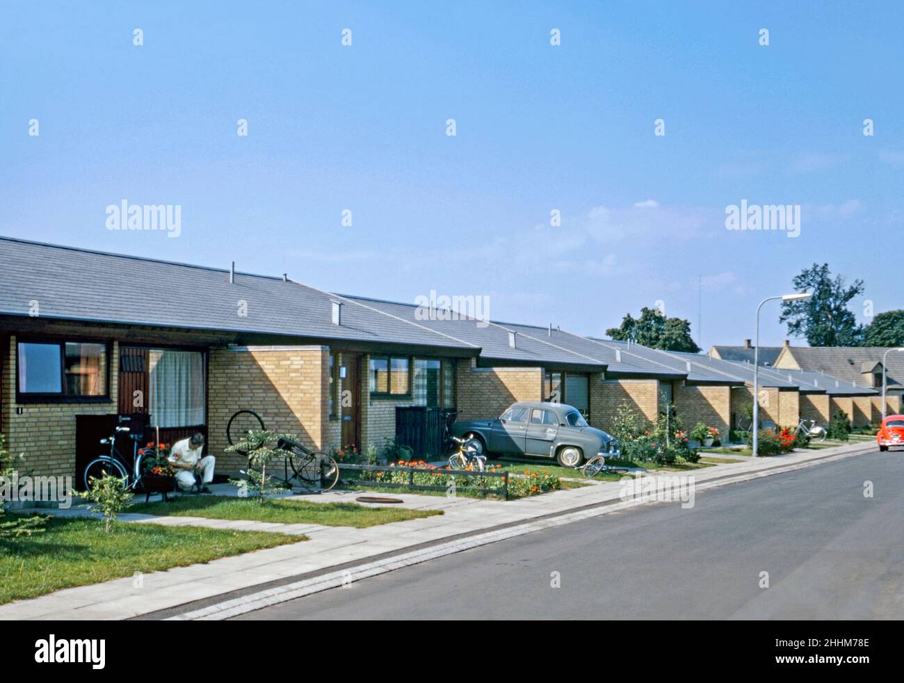 Single-storey housing in a development of post-war modern houses in Odense, Funen, Denmark in 1970. Odense is the third-largest city in Denmark and is the main city of the island of Funen. One man is repairing bicycles in his driveway. This image is from an amateur 35mm Kodak colour transparency – a vintage 1970s photograph. Stock Photo