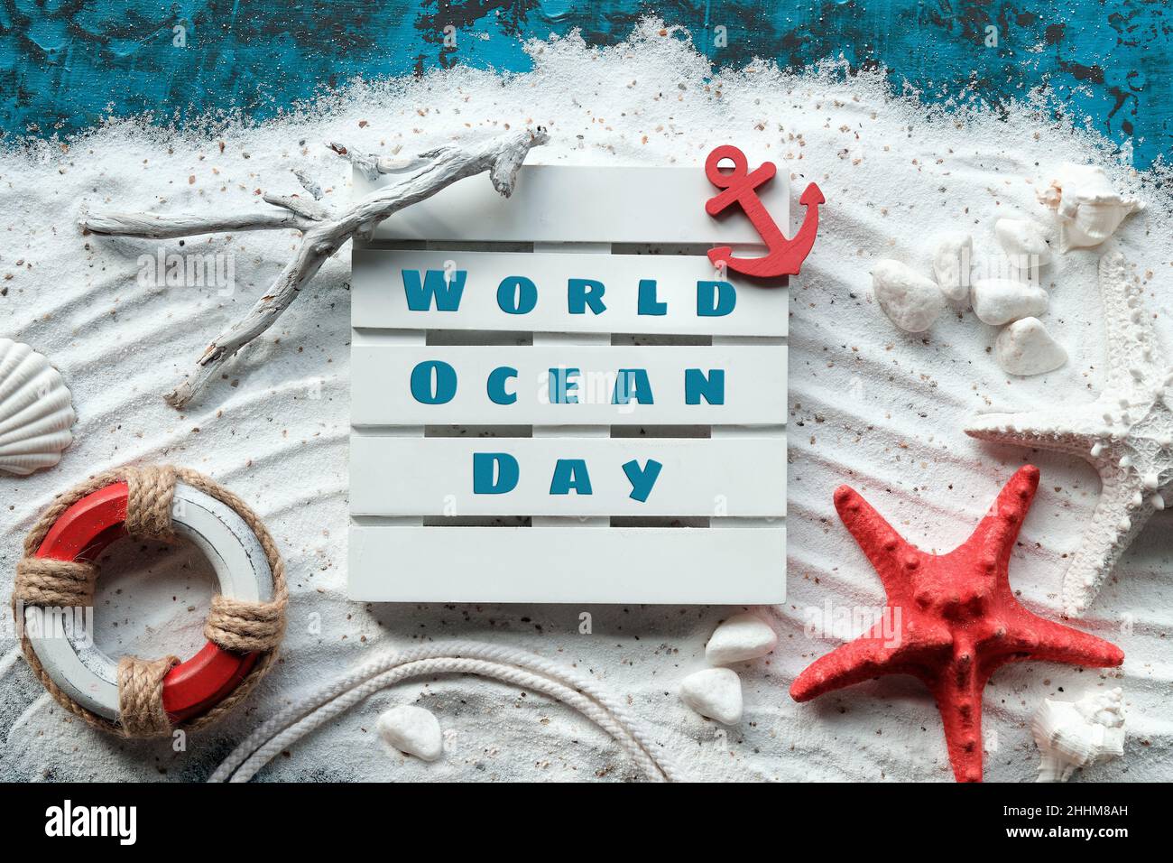 World Oceans Day text. Background with white sand on turquoise blue. Shells, red starfish, anchor. Stock Photo