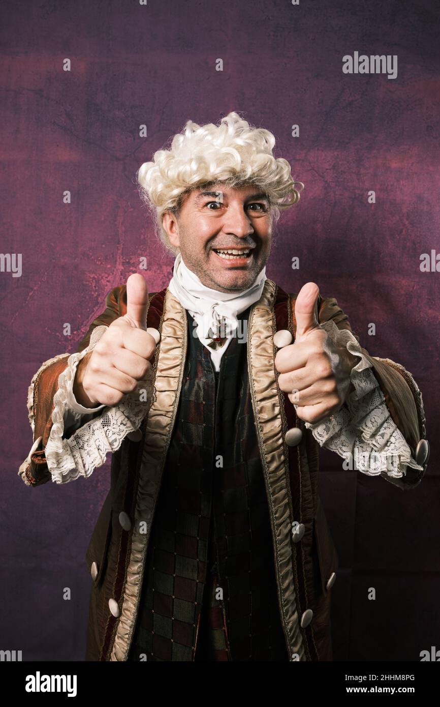 Man in classic medieval clothes showing thumbs up to the camera while posing on isolated background. Stock Photo