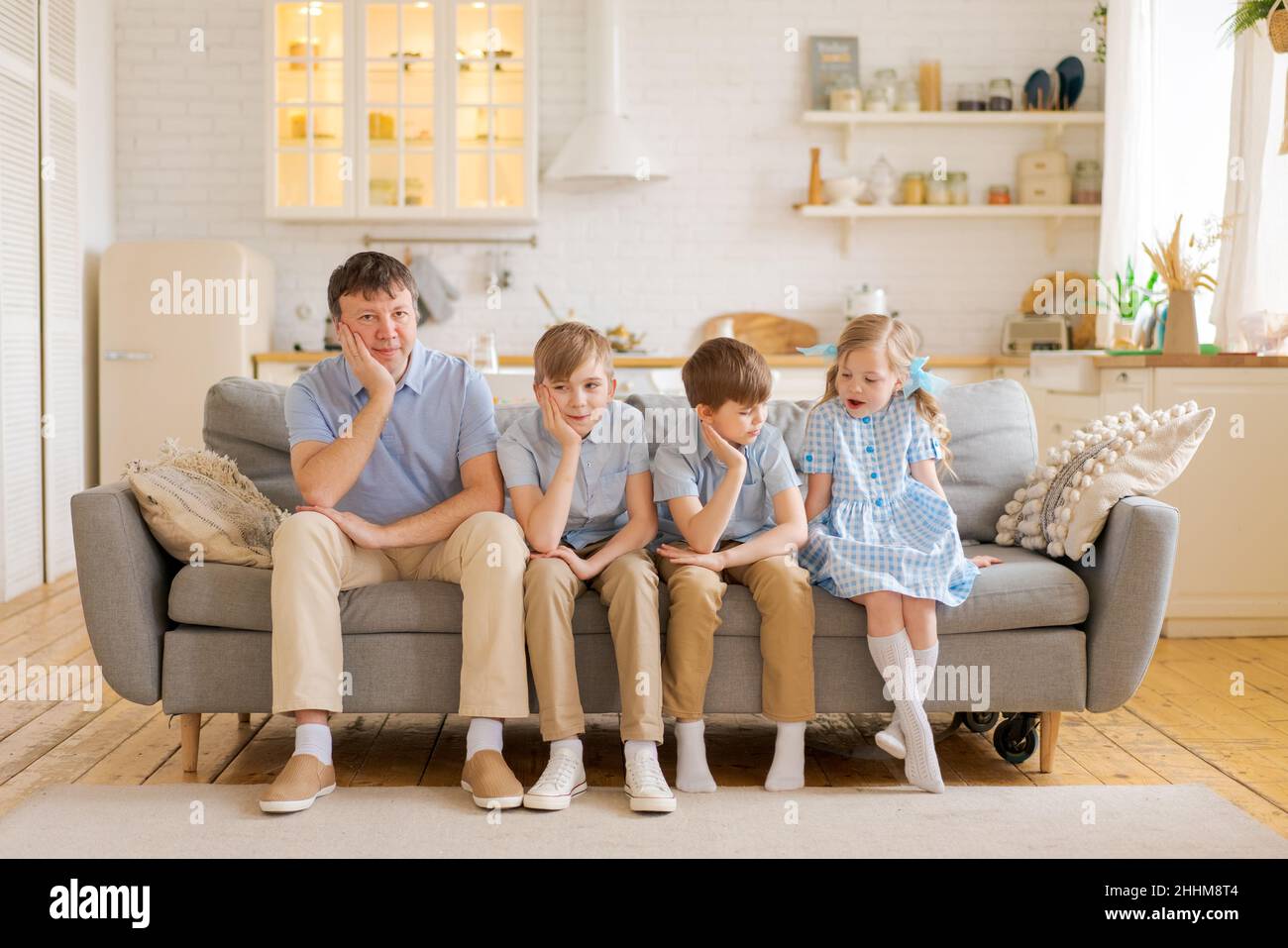 Happy dad and little kids laughing at funny humorous comedy movie or tv show sitting at home on sofa in living room kitchen smiling father having fun with kids watching tv together at weekend Stock Photo