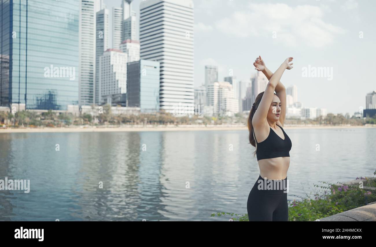 Sport woman wearing wireless headphones and stretching muscles before running in city, warmup exercise. Stock Photo