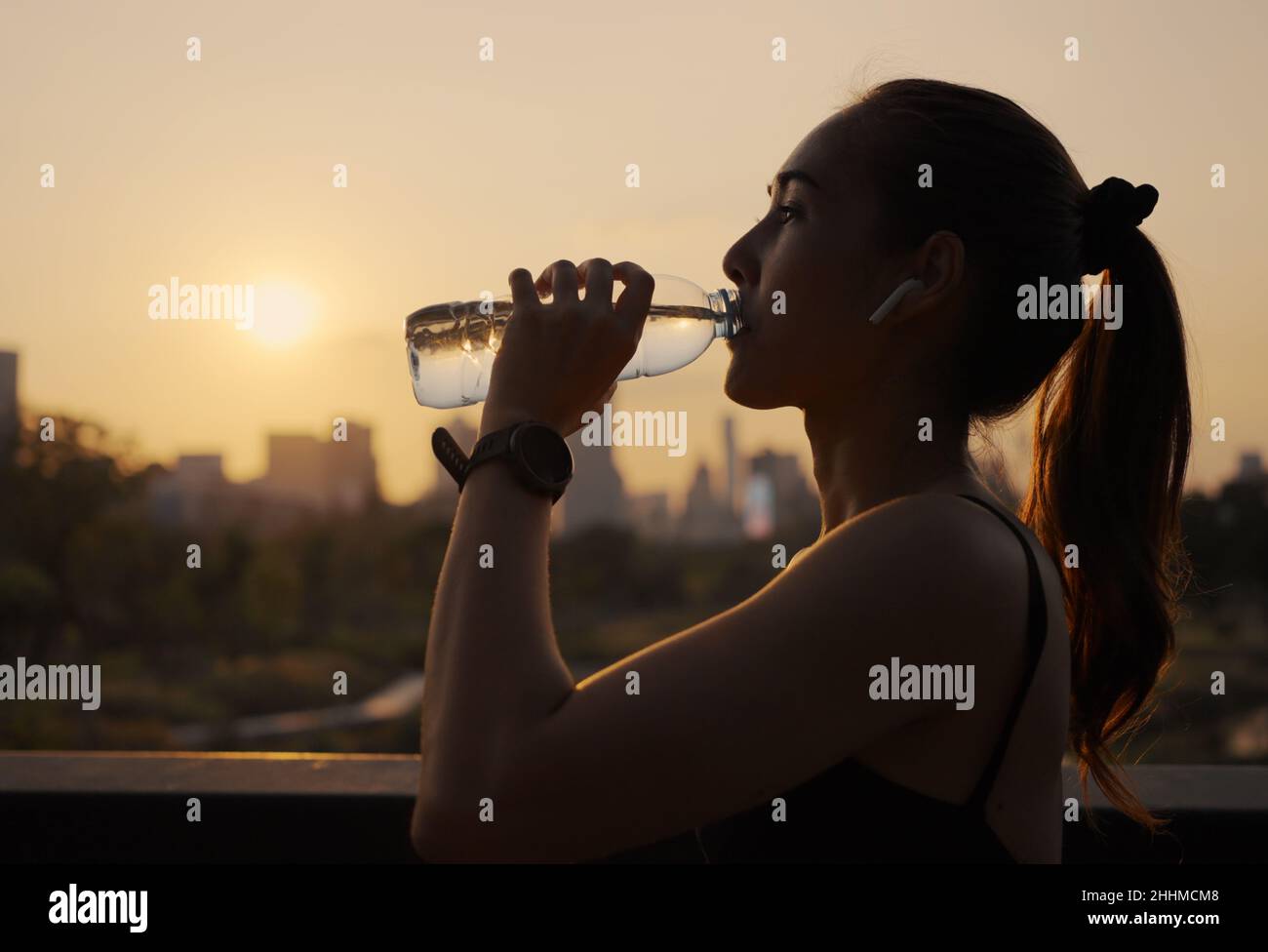 Young woman drinking water after jogging at sunset. Stock Photo