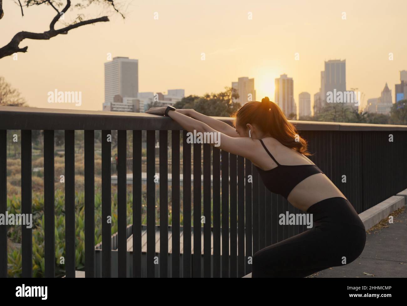 Young woman in sportswear streching on the bridge in the city at sunset. Stock Photo