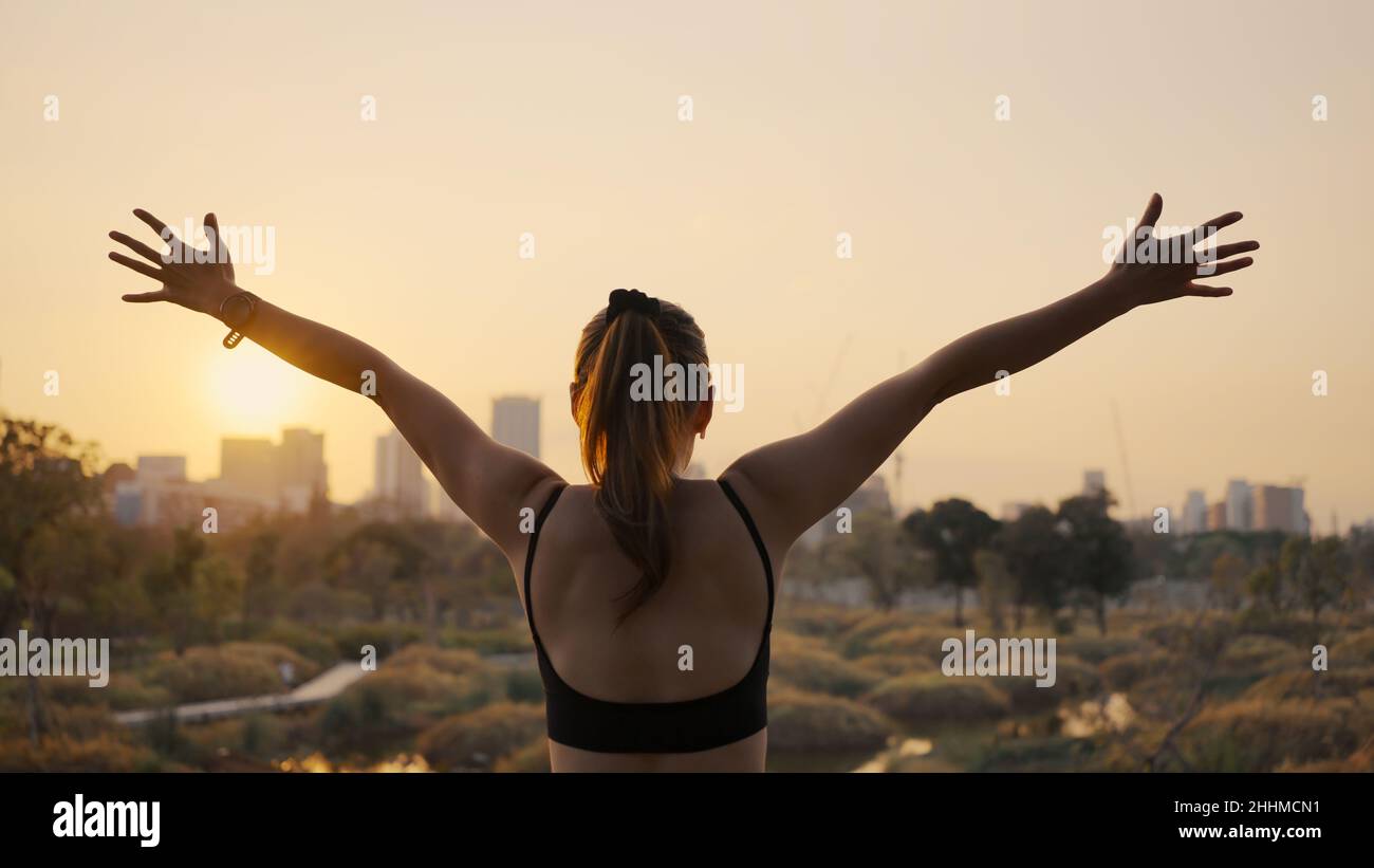 Young woman outstretched arms and standing in the city at sunset. Stock Photo