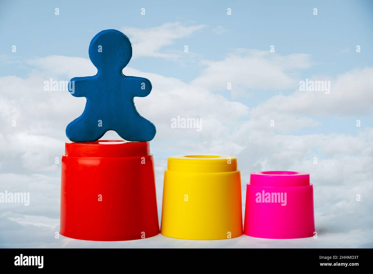 A plasticine man standing on the highest podium against a trendy background of a blue sky with clouds. Leadership concept. Stock Photo