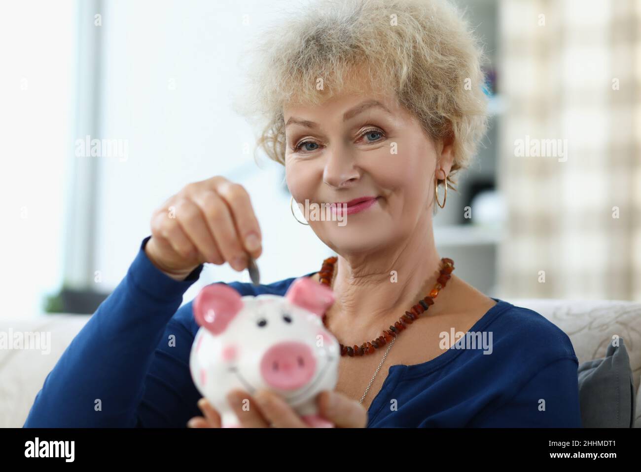 An elderly woman puts a coin in a piggy bank Stock Photo - Alamy