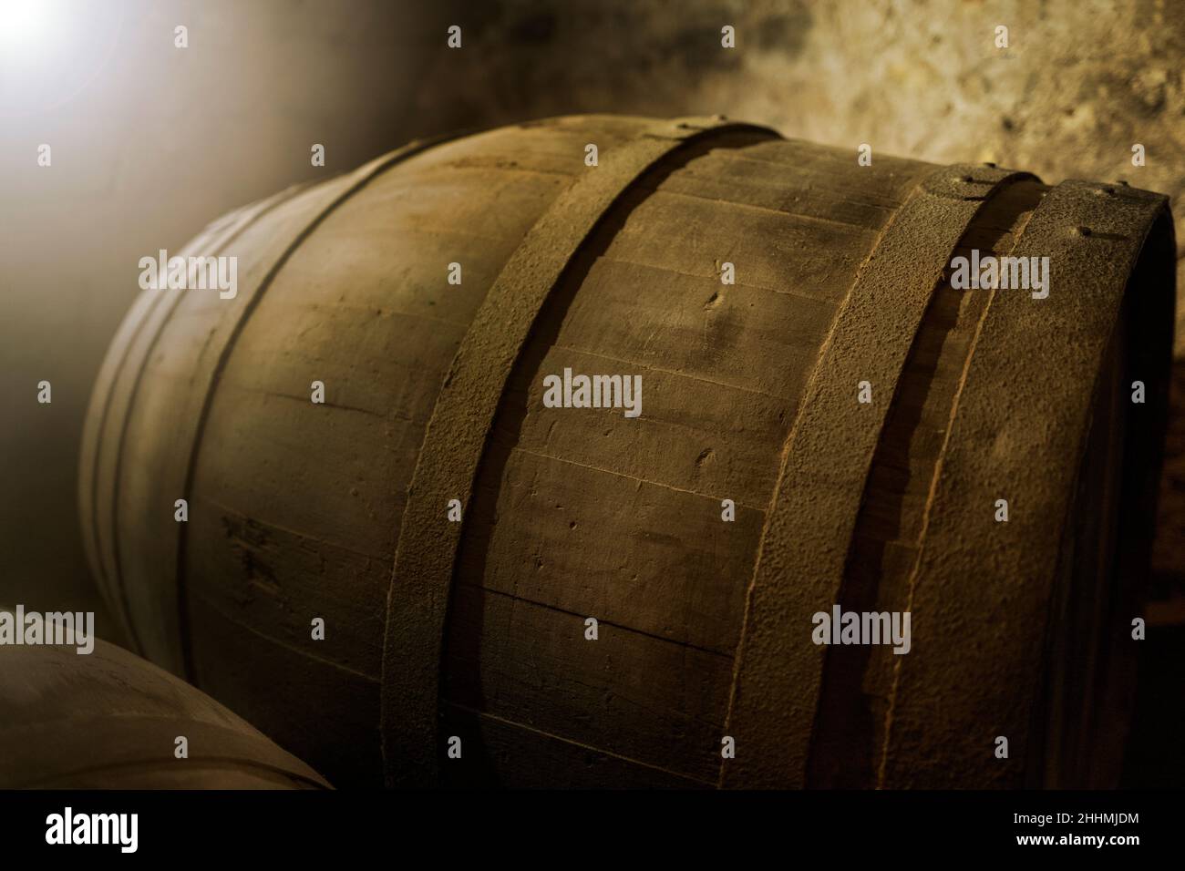 Shallow focus against very ancient wine barrel in dark and warm cellar ambiance with light effect. Usefull banner Stock Photo