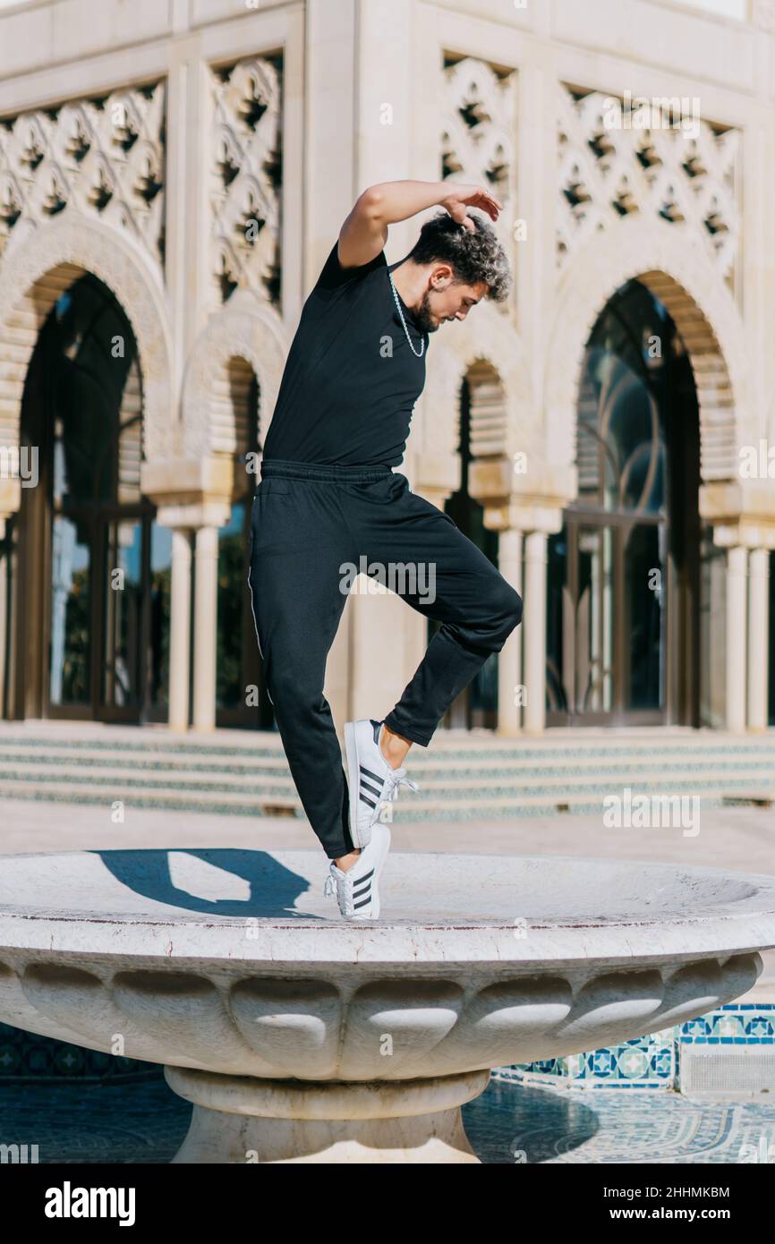 Young Spanish man with hair highlights breakdancing on a fountain outdoors Stock Photo