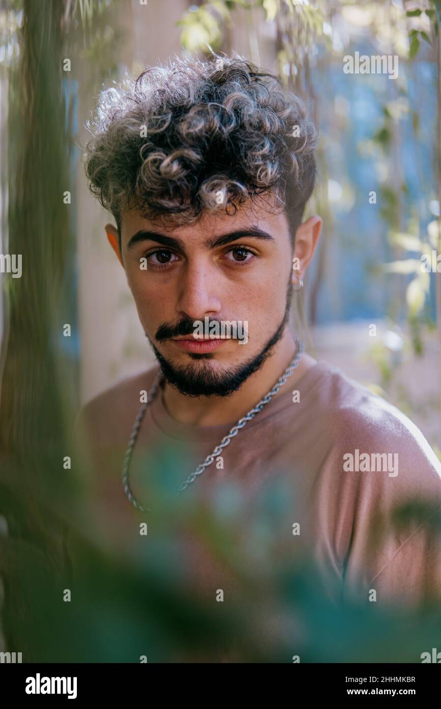 Portrait of an attractive young Spanish man with hair highlights and beard in a garden Stock